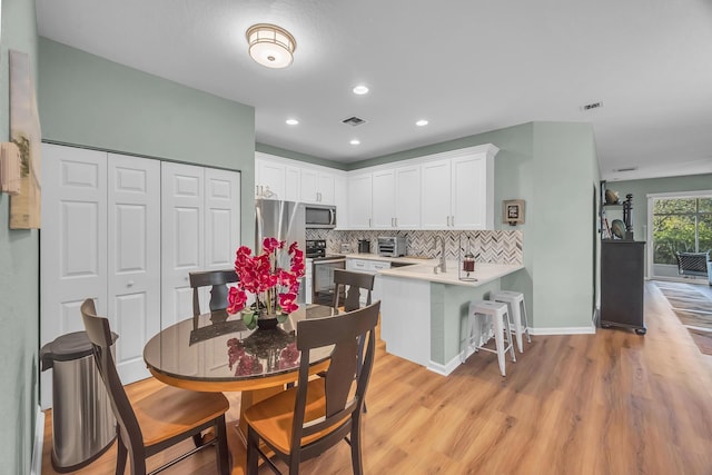 kitchen featuring white cabinets, light wood-type flooring, tasteful backsplash, kitchen peninsula, and stainless steel appliances