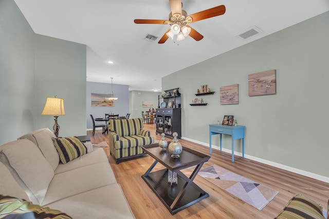 living room with ceiling fan with notable chandelier and light hardwood / wood-style flooring