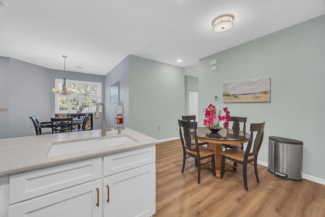 kitchen featuring light stone counters, sink, pendant lighting, white cabinets, and light hardwood / wood-style floors