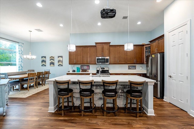 kitchen with hanging light fixtures, a center island with sink, appliances with stainless steel finishes, and dark hardwood / wood-style flooring