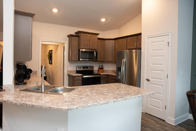 kitchen featuring sink, light stone counters, dark hardwood / wood-style flooring, kitchen peninsula, and appliances with stainless steel finishes