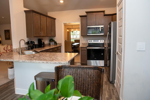 kitchen with kitchen peninsula, appliances with stainless steel finishes, dark hardwood / wood-style flooring, a kitchen breakfast bar, and sink