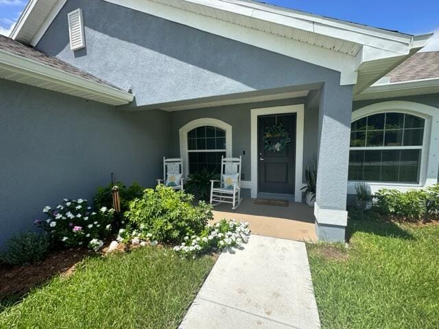 view of exterior entry featuring a yard and a porch