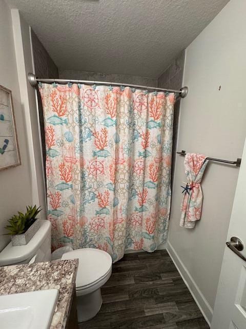 bathroom featuring curtained shower, toilet, wood-type flooring, and a textured ceiling