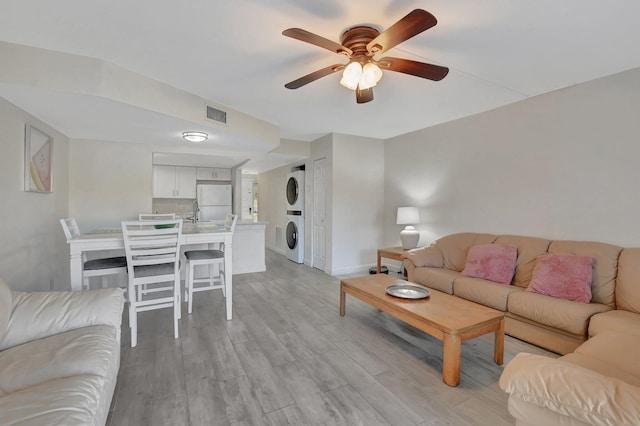 living room featuring stacked washer and dryer, ceiling fan, and light hardwood / wood-style floors