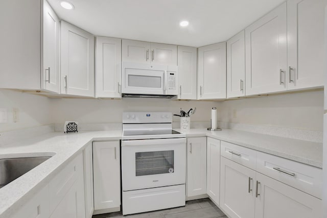 kitchen with white cabinetry, sink, light stone counters, and white appliances