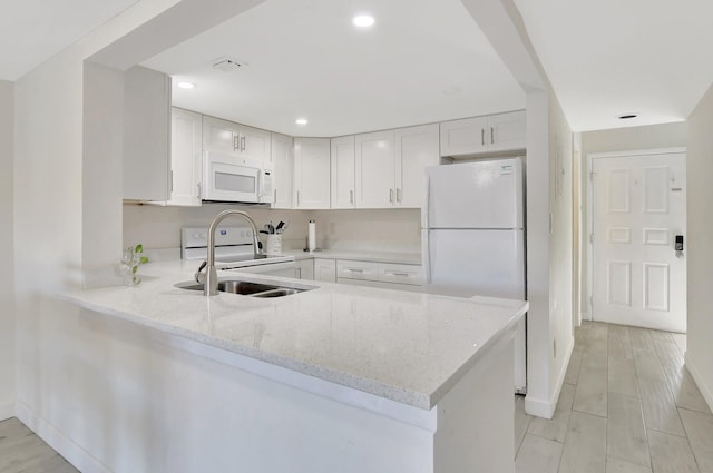 kitchen with kitchen peninsula, light stone countertops, light wood-type flooring, white appliances, and white cabinetry