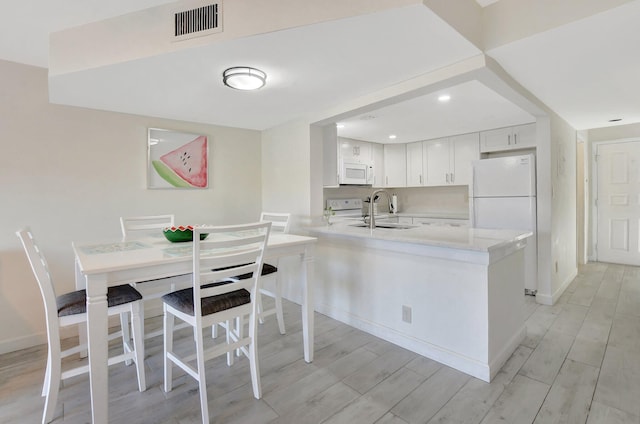 kitchen with kitchen peninsula, white appliances, sink, light hardwood / wood-style flooring, and white cabinetry