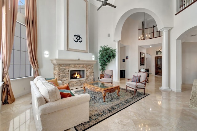 living room featuring ceiling fan, a healthy amount of sunlight, a stone fireplace, and a towering ceiling