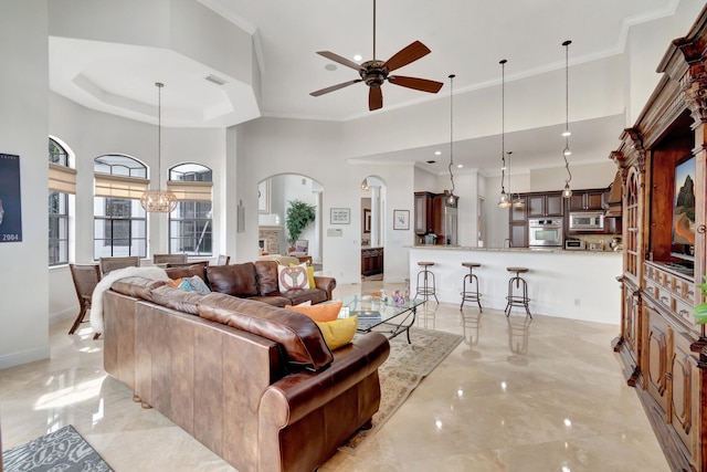 living room featuring a raised ceiling, crown molding, a high ceiling, and ceiling fan with notable chandelier