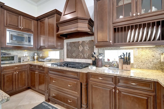 kitchen with stainless steel microwave, crown molding, tasteful backsplash, custom range hood, and gas cooktop