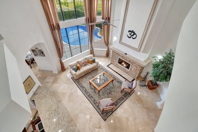 living room featuring ceiling fan, a stone fireplace, and a high ceiling