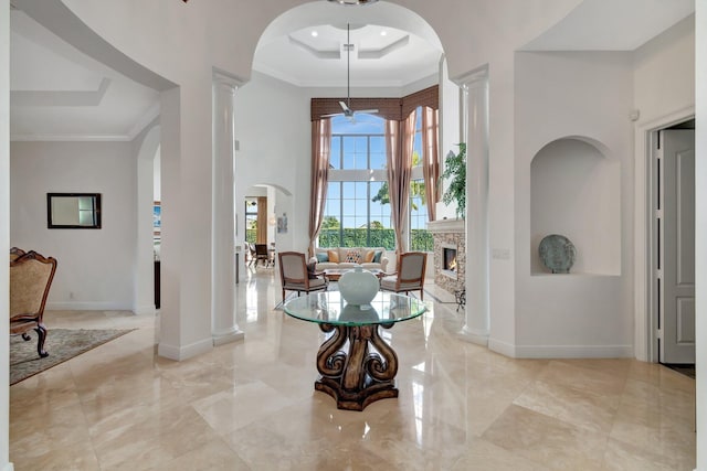 foyer entrance featuring a raised ceiling, ornamental molding, a fireplace, a towering ceiling, and ornate columns