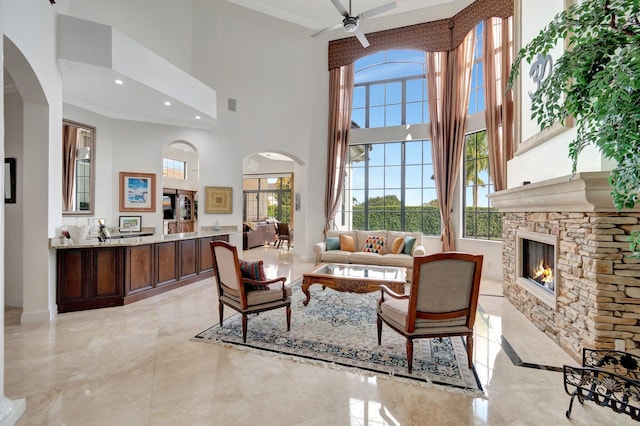 living room featuring ceiling fan, a fireplace, and a high ceiling