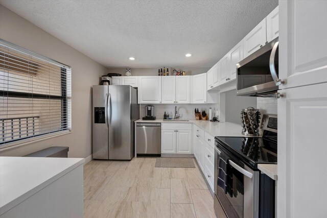 kitchen featuring sink, appliances with stainless steel finishes, white cabinetry, a textured ceiling, and decorative backsplash