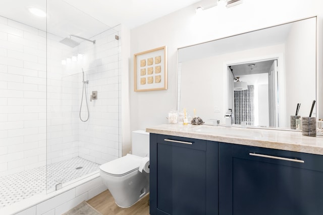 bathroom featuring toilet, vanity, wood-type flooring, and tiled shower