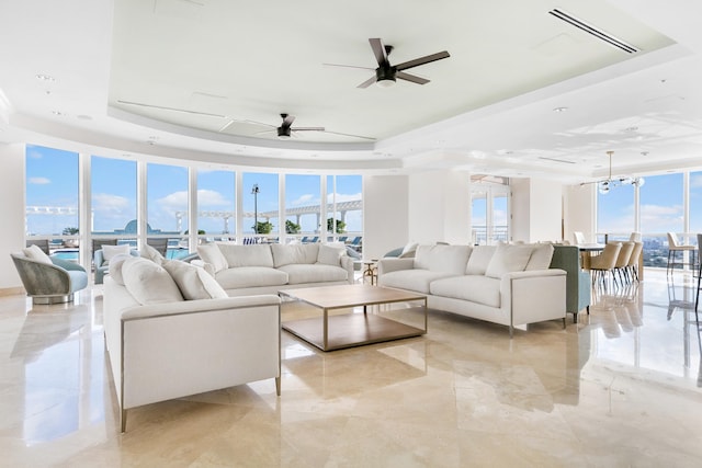 living room with ceiling fan with notable chandelier, a tray ceiling, and expansive windows