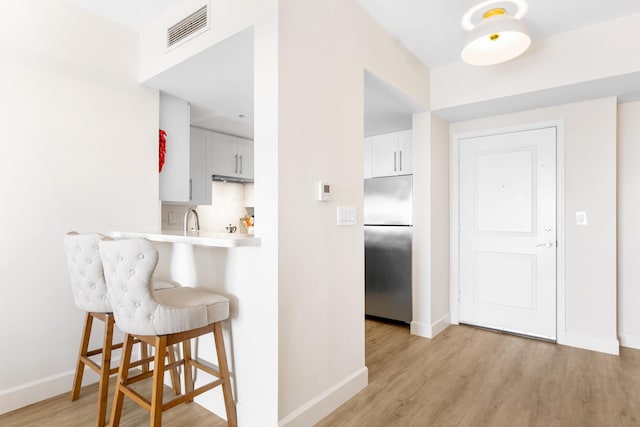 kitchen featuring sink, light wood-type flooring, a kitchen breakfast bar, white cabinets, and stainless steel fridge