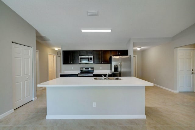 kitchen with light tile patterned flooring, stainless steel appliances, a kitchen island with sink, and sink