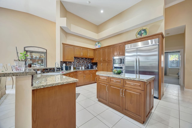 kitchen featuring sink, light tile patterned floors, built in appliances, light stone counters, and kitchen peninsula