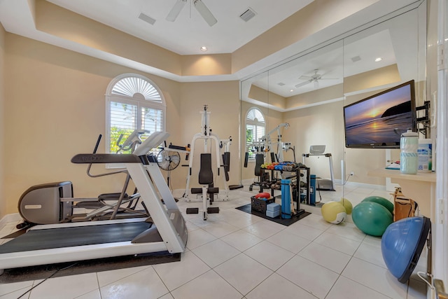 exercise room with ceiling fan, a raised ceiling, and light tile patterned floors