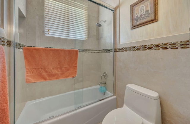 bathroom featuring combined bath / shower with glass door, tile walls, and toilet