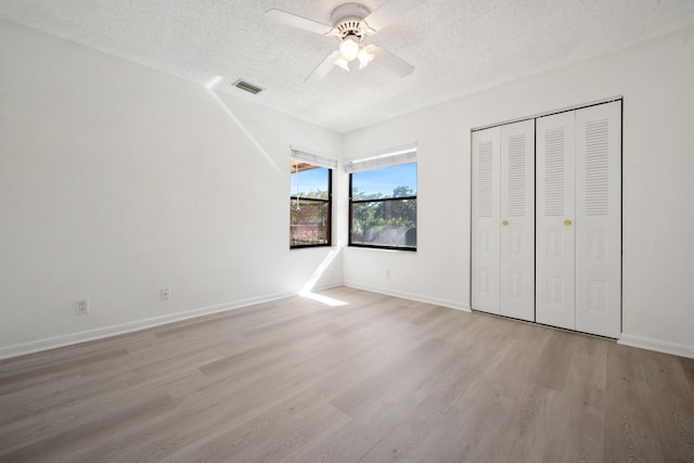 unfurnished bedroom with ceiling fan, light hardwood / wood-style floors, a textured ceiling, and a closet