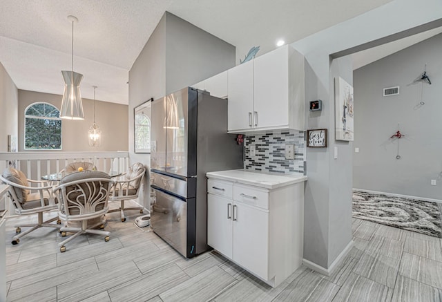 kitchen featuring stainless steel refrigerator, white cabinetry, tasteful backsplash, vaulted ceiling, and decorative light fixtures