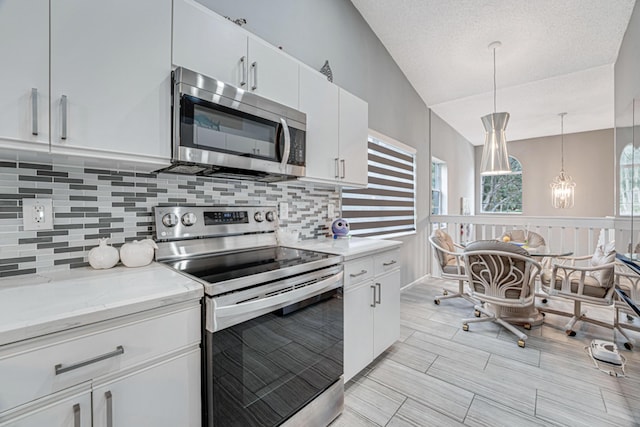 kitchen with tasteful backsplash, decorative light fixtures, vaulted ceiling, white cabinets, and appliances with stainless steel finishes