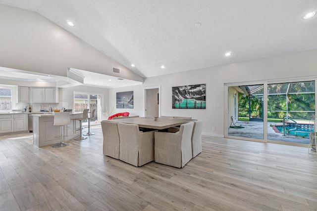 living room with light hardwood / wood-style flooring, high vaulted ceiling, and a textured ceiling