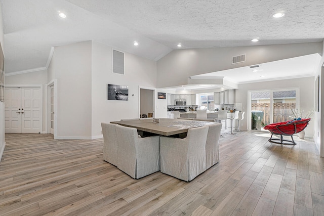 dining room with vaulted ceiling, light hardwood / wood-style flooring, a textured ceiling, and ornamental molding