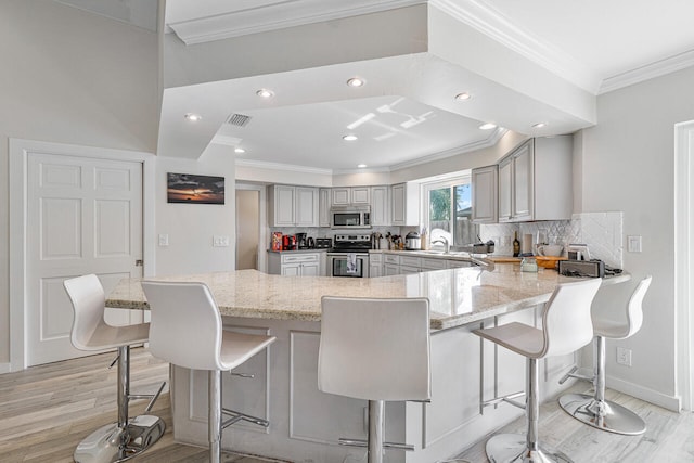 kitchen featuring a breakfast bar, stainless steel appliances, kitchen peninsula, and gray cabinetry