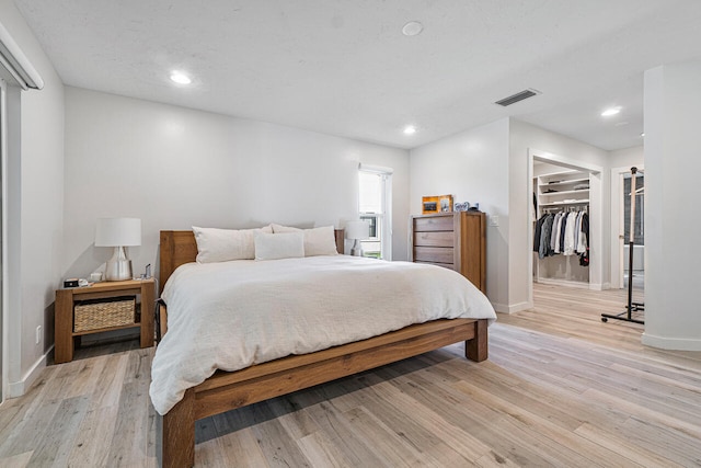 bedroom featuring a walk in closet, light hardwood / wood-style flooring, and a closet