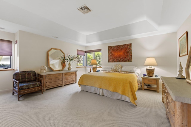 bedroom featuring a raised ceiling, light colored carpet, and visible vents