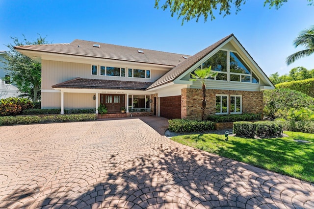 view of front of home with decorative driveway, brick siding, an attached garage, and a front yard