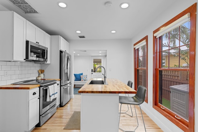 kitchen with appliances with stainless steel finishes, wood counters, a kitchen breakfast bar, sink, and a center island with sink