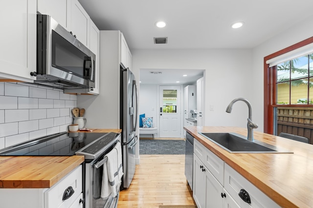 kitchen featuring appliances with stainless steel finishes, wood counters, white cabinetry, sink, and plenty of natural light