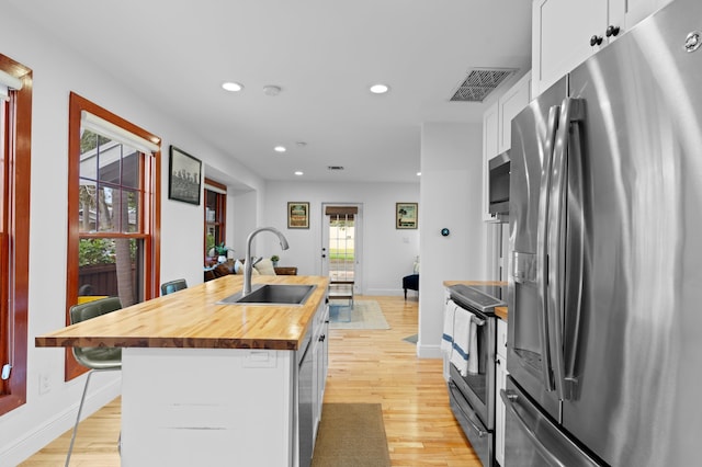 kitchen with appliances with stainless steel finishes, wood counters, white cabinetry, sink, and a kitchen island with sink