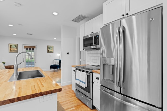 kitchen with white cabinets, appliances with stainless steel finishes, wooden counters, sink, and backsplash