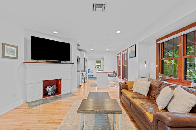 living room with light wood-type flooring, a fireplace, and sink