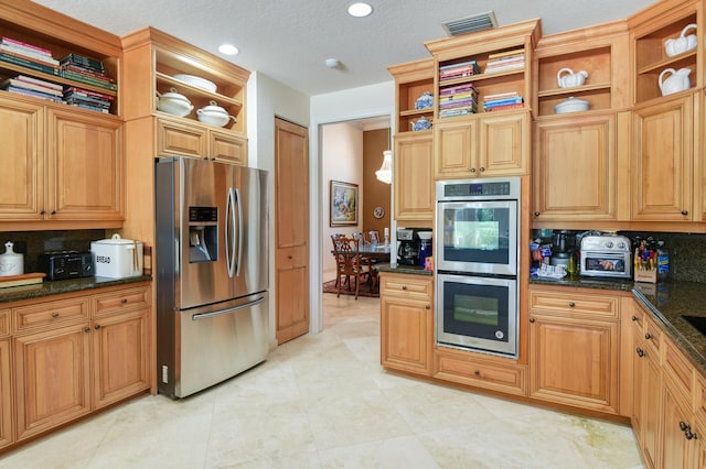 kitchen featuring backsplash, appliances with stainless steel finishes, a textured ceiling, and dark stone countertops