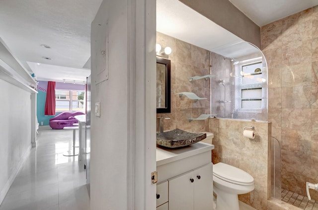 bathroom with tiled shower, vanity, toilet, and tile walls