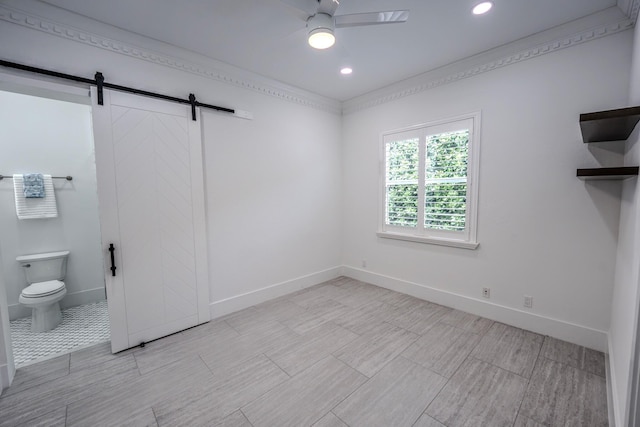 interior space featuring ceiling fan, a barn door, and ornamental molding