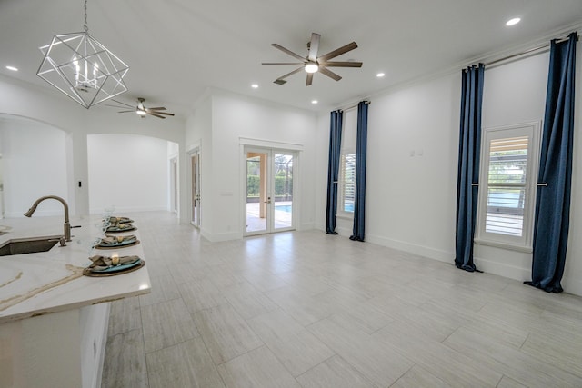 unfurnished living room with crown molding, french doors, ceiling fan with notable chandelier, and sink