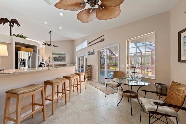 kitchen featuring light stone countertops, vaulted ceiling, ceiling fan, light tile patterned floors, and stainless steel fridge with ice dispenser