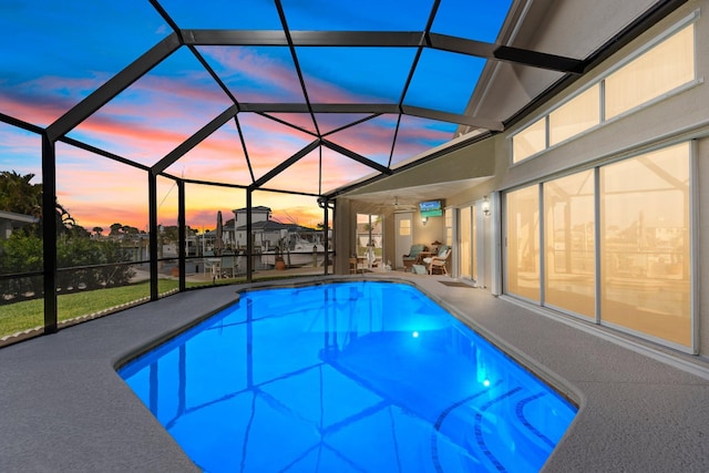 pool at dusk with glass enclosure and a patio area