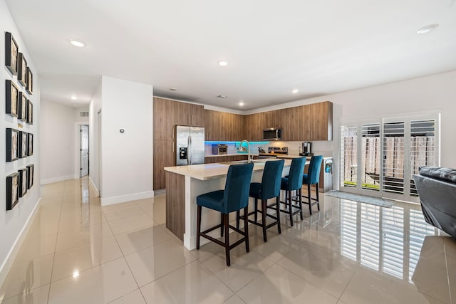 kitchen featuring wood walls, a kitchen breakfast bar, an island with sink, light tile patterned flooring, and stainless steel appliances