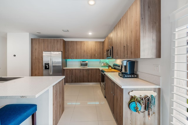 kitchen with sink, light tile patterned floors, a breakfast bar area, and appliances with stainless steel finishes