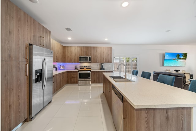 kitchen featuring sink, an island with sink, light tile patterned floors, and appliances with stainless steel finishes