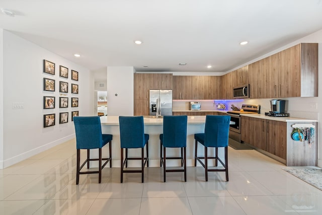 kitchen with a breakfast bar area, a kitchen island, light tile patterned floors, and appliances with stainless steel finishes